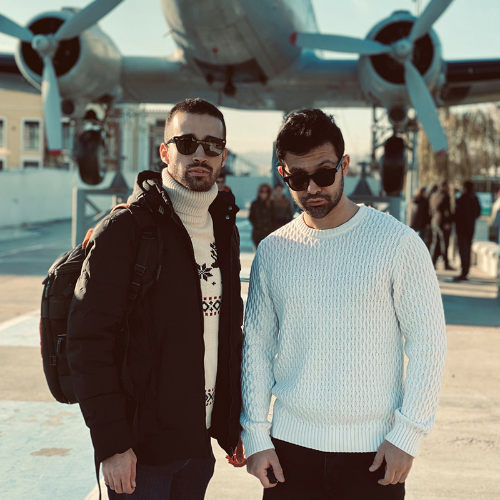 Two men are standing in front of a display airplane wearing mens sunglasses while posing for a camera.