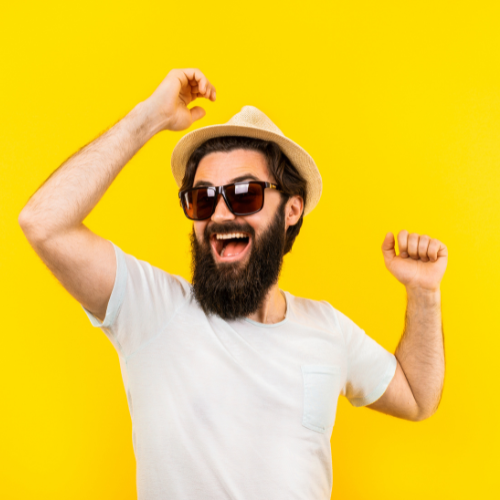 A man is jumping up and down in excitement in front of a yellow background while wearing a black pair of sunglasses. 