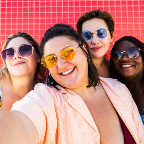 A group of four women are wearing various styles of womens sunglasses while posing for a picture. 