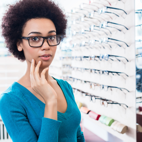 A lady is in an eyewear store wearing a pair of black clear lens glasses.